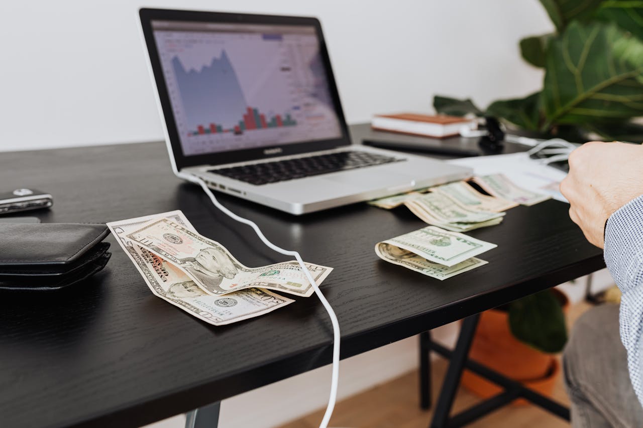 A workspace with cash, laptop, and financial graph showing investment analysis.