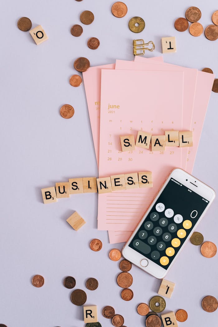 Flat lay with coins, smartphone, and SMALL BUSINESS tiles on a planner.